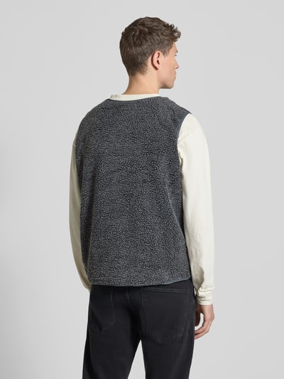 Mannenmodel draagt Straight fit bodywarmer met logopatch Model 'Hoktown' van American Vintage in imitatiebont, ruglengte maat M/L 64 cm, schouderbreedte 44 cm, borstwijdte 62 cm, kleur grijs, ganzekörperaanzicht achterzijde.
