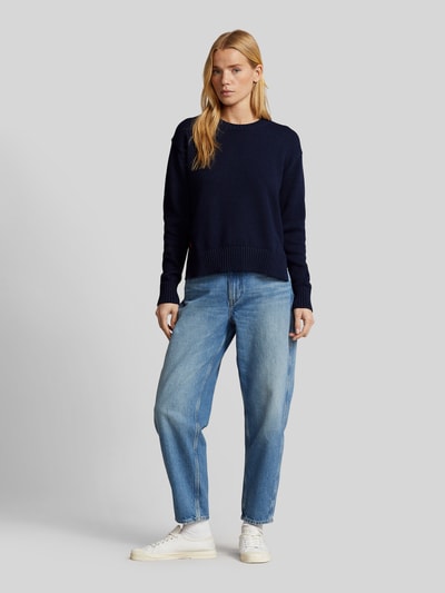Frauenmodel trägt Regular Fit Strickpullover aus reiner Baumwolle von Polo Ralph Lauren in Dunkelblau, unifarben, Logo-Stitching, Crew Neck, gerippte Abschlüsse, kombiniert mit blauer Jeans und weißen Sneakern, Stricktextur, Ganzkörperansicht von vorne.