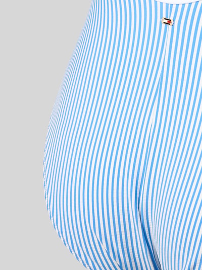 Frauenmodel trägt Badeanzug mit Logo-Stitching von TOMMY HILFIGER, blau-weißes Allover-Muster, Crinkle-Struktur, Nahaufnahme Hüfte.