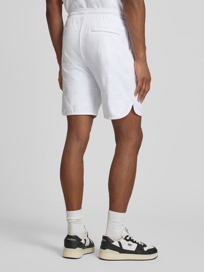Mężczyznamodel nosi Regular Fit Shorts aus Baumwoll-Mix Modell 'JT_Member Short' od BOSS Green, biały kolor, materiał bawełniany, wzór graficzny, krój regular fit, elastyczny pas, kieszenie boczne, imitacja tylnej kieszeni, tekstura sweat, widok całej sylwetki z tyłu.