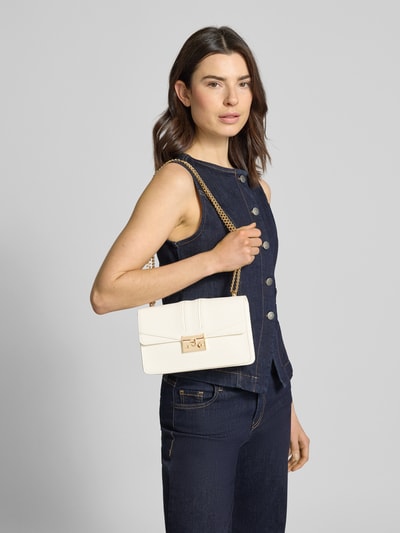 Frauenmodel trägt Crossbody-Bag in Leder-Optik Modell 'Roros East-West' von Seidenfelt, cremefarben, Struktur, Ketten-Optik, Nahaufnahme Oberkörper. Hauptfach mit Überschlag, Reißverschlussfach, Maße: 23 cm Breite, 15 cm Länge, 7 cm Tiefe, Schulterriemen 115 cm.