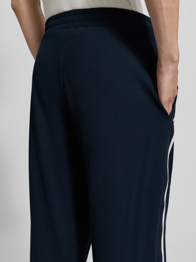 Männermodel trägt Trackpants aus viscosemix von EA7 Emporio Armani in donkerblauw met galonstrepen, steekzakken en labelprint, detailaufnahme