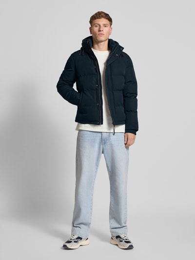 Männermodel trägt dunkelblaue Steppjacke mit Eingrifftaschen Modell 'Everest' von Superdry, Regular-Fit, Kapuze, Label-Detail, Ganzkörperansicht von vorne, Rückenlänge bei Größe M 66 cm, Schulterbreite 48 cm, Brustweite 42 cm, Ärmellänge 70 cm.