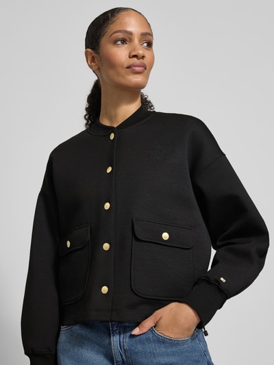 Frauenmodel trägt Regular Fit Bomberjacke aus Baumwoll-Mix Modell 'GOLD BUTTON BOMBER' von Tommy Hilfiger in Schwarz mit goldenen Knöpfen, zwei Pattentaschen, College-Kragen und Logo-Stitching, Nahaufnahme Oberkörper.