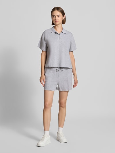 Frauenmodel trägt Relaxed Fit Poloshirt mit Strukturmuster Modell 'Noa' von OH APRIL in Hellgrau, glatte Textur, Ganzkörperansicht von vorne. Damen Poloshirt, Knopfleiste, Rückenlänge bei Größe S: 55 cm.
