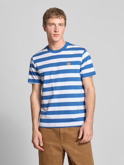 Männermodel trägt T-Shirt mit Label-Stitching Modell 'RIVERGROVE' von Dickies aus reiner Baumwolle, blau-weiß gestreift, Regular Fit, Nahaufnahme Oberkörper.