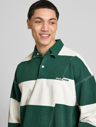 Mężczyznamodel nosi koszulkę polo Relaxed Fit Poloshirt aus reiner Baumwolle Modell 'Castelluccio' von Pegador, bawełna, krój relaxed fit, kołnierzyk polo z listwą guzikową, ściągacze na rękawach, wyhaftowane logo, obniżone ramiona, długość tyłu w rozmiarze M: 69 cm, szerokie zielono-kremowe pasy, tekstura gładka, widoczne logo, zbliżenie na górną część ciała, widok z przodu.