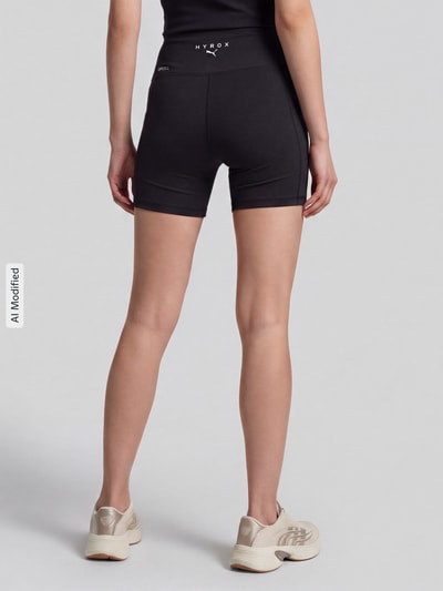 Frauenmodel trägt schwarze Elastische Sportshorts mit Logo-Print Modell 'PUMA X HYROX ESS SHORT' von PUMA, Damen Sportshorts, Ganzkörperansicht Rückansicht, KI-modifiziertes Bild.