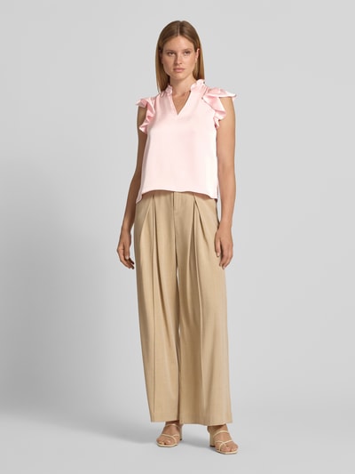 Frauenmodel trägt Blusentop aus Satin Modell 'Stella' von Neo Noir in zartem Rosa mit Rüschen, V-Ausschnitt und Stehkragen, Ganzkörperansicht von vorne. Material-Mix mit Stretch-Anteil, Regular Fit, Rückenlänge 58 cm, Ärmellänge 9 cm.