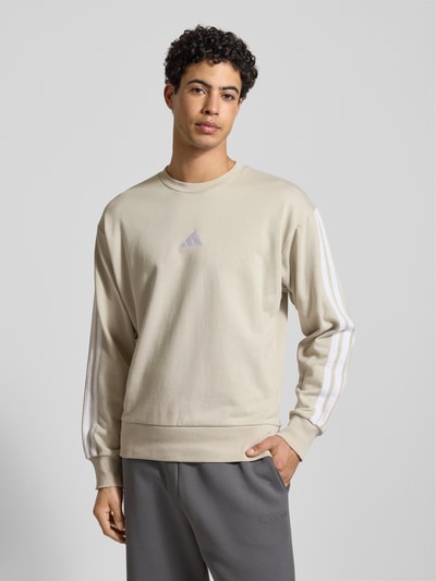 Männermodel trägt Sweatshirt mit Label-Stitching von adidas Sportswear, Baumwoll-Mix mit Viskose-Anteil, lockerer Schnitt, Rundhalsausschnitt, gerippte Abschlüsse, Rückenlänge 68 cm, Ärmellänge 62 cm, helle Farben, weiche Textur, Ganzkörperansicht von vorne.