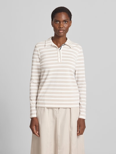 Frauenmodel trägt Longsleeve im Allover-Look mit Polokragen und Knopfleiste von Marc Cain, schimmernde Streifen in Beige und Weiß, Regular Fit, Material-Mix mit Stretch-Anteil, dezente Knopfleiste, kombiniert mit hellbeigem Rock, Ganzkörperansicht von vorne.