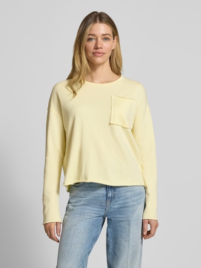 Frauenmodel trägt Sweatshirt mit Brusttasche von Rich & Royal in Hellgelb aus Reine Bio-Baumwolle, Loose-Fit, Rundhalsausschnitt, ausgefranster Saum, überschnittene Schultern, Ganzkörperansicht von vorne.