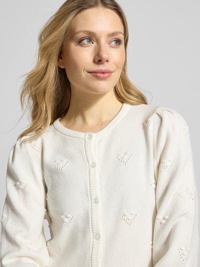 Vrouwenmodel draagt Strickjacke aus Viskose-Mix mit Knopfleiste Modell 'MANINA' van B.Young, wit met hartjesstructuur, getailleerde pasvorm, ribboorden, ronde hals, doorlopende knoopsluiting, mix van viscose met stretch. Nahaufnahme bovenlichaam.