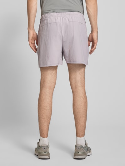 Männermodel trägt Shorts mit elastischem Bund und Logo von New Balance in Hellviolett, Regular Fit, Detail des Tunnelzugs, Ganzkörperansicht Rückansicht.