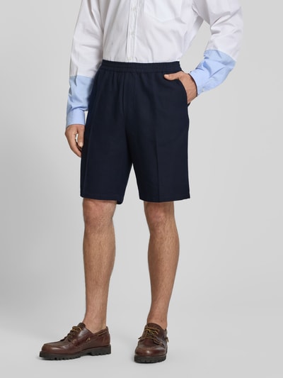 Männermodel trägt dunkelblaue Straight Fit Shorts aus Leinen-Mix von Filippa K mit elastischem Bund und Bügelfalten, Nahaufnahme Oberschenkel, Kontext: Herren Shorts, Baumwoll-Anteil, Eingriff- und Gesäßtaschen, Innenbeinlänge 24 cm, Bundweite 43 cm.