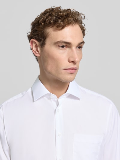 Männermodel trägt Regular Fit Business-Hemd mit Kentkragen von SEIDENSTICKER, reine Baumwolle, weiß, sichtbare Brusttasche, Knopfleiste, Nahaufnahme Oberkörper.