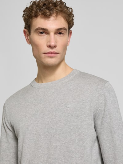 Męski model nosi Regular Fit Strickpullover aus reiner Baumwolle od Tom Tailor w jednolitym jasnoszarym kolorze, dzianina, długi rękaw, logo, okrągły dekolt, krój regular fit, detal: żebrowane wykończenia, zdjęcie: zbliżenie na górną część ciała.