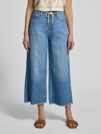 Frauenmodel trägt Wide Leg Culotte-Jeans aus Lyocell-Baumwoll-Mix Modell 'SURI' von s.Oliver RED LABEL, hellblauer Denim, 5-Pocket, Fransen, Nahaufnahme Oberkörper bis Knöchel.