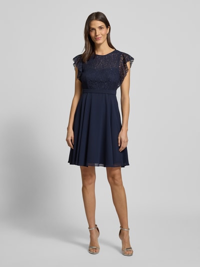 Frauenmodel trägt Knielanges Cocktailkleid mit Rundhalsausschnitt von Jake*s Cocktail, taillierter Schnitt, blickdichtes Unterkleid, Nahtreißverschluss, dunkelblau, Ganzkörperansicht von vorne. Rückenlänge bei Größe 36: 90 cm, Brustweite 35 cm, Ärmellänge 10 cm.
