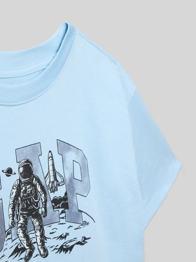 Mädchen trägt T-Shirt mit Motiv- und Logo-Print von GAP in Hellblau, Reine Baumwolle, Gerippter Rundhalsausschnitt, Nahaufnahme Oberkörper.