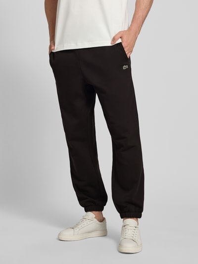 Męski model nosi Regular Fit Sweatpants aus Baumwoll-Mix von Lacoste, efekt: jednolity kolor, mieszanka bawełny, wpuszczane kieszenie, wyhaftowane logo, krój regular fit, elastyczny tunel, ściągacze nogawek, dzianina dresowa, polar szczotkowany, widok całej sylwetki z przodu.