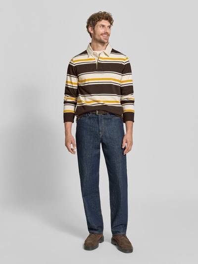 Mannenmodel draagt Regular Fit poloshirt uit puur katoen van GANT in bruin, geel en wit met brede strepen, donkerblauwe jeans, geheellichaamsaanzicht van voren.