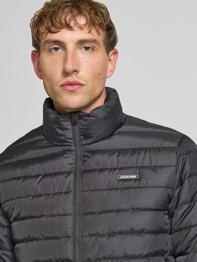 Männermodel trägt Jacke mit Label-Patch Modell 'ELVIS' von JACK & JONES, gesteppter Stoff, dunkelgrau, Nahaufnahme Oberkörper. Rückenlänge 67 cm, Schulterbreite 49 cm, Brustweite 56 cm, Ärmellänge 67 cm, gerader Schnitt, Stehkragen, Reißverschluss, seitliche Reißverschlusstaschen.
