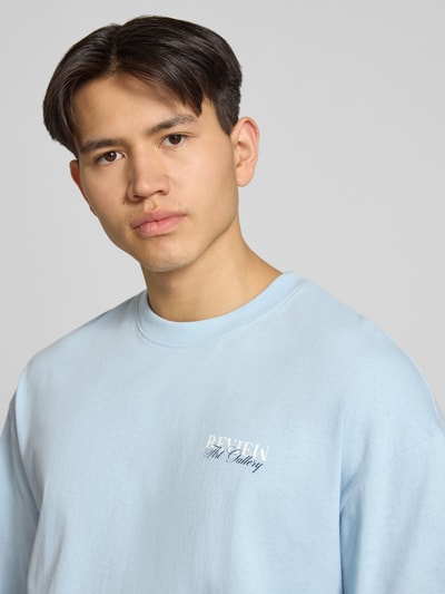 Männermodel trägt T-Shirt mit Label-Detail von REVIEW in Hellblau, Baumwolle, lockerer Schnitt, Nahaufnahme Oberkörper.