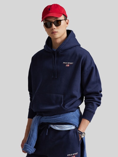 Männermodel trägt Relaxed Fit Hoodie aus Baumwoll-Mix von Polo Ralph Lauren, dunkelblau unifarben, Label-Schriftzug, Nahaufnahme Oberkörper.