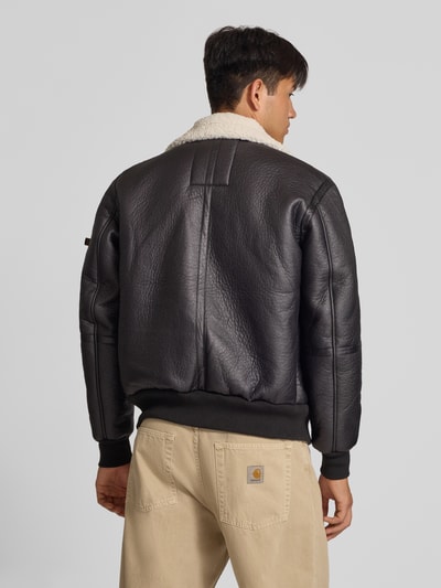 Männermodel trägt Bomberjacke mit Label-Patch und Kentkragen von Alpha Industries, schwarze Lederoptik, Rückansicht, Ganzkörperansicht Rückansicht. Rückenlänge, Schulterbreite, Brustweite und Ärmellänge gemäß Kontext.