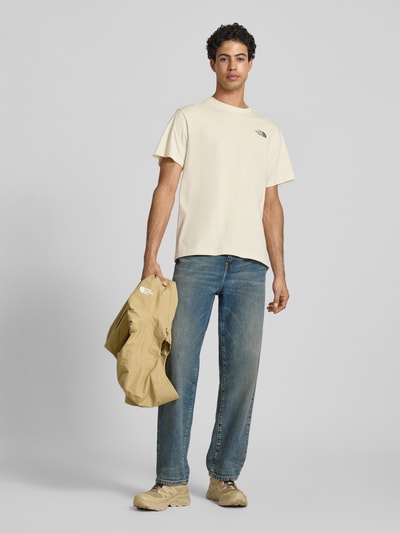 Męski model nosi Relaxed Fit T-Shirt mit Logo-Print von The North Face z bawełny, okrągły dekolt, długość tyłu 70 cm w rozmiarze M, jasne kolory, gładka faktura, Ganzkörperansicht von vorne.
