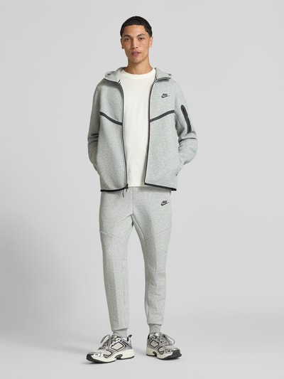 Männermodel trägt Regular Fit Sweatjacke aus Baumwoll-Mix von Nike in Hellgrau mit schwarzen Details, Ganzkörperansicht von vorne. Herren Sweatjacke von Nike.
