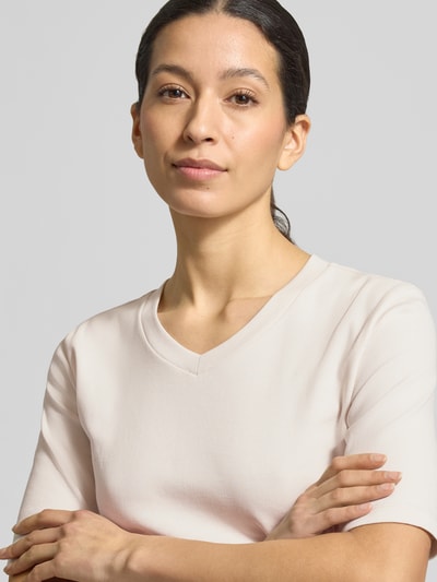 Kobiece modelka ma na sobie T-shirt mit V-Ausschnitt von Christian Berg Woman, mieszanka bawełny i elastanu, krój regular fit, dekolt w serek, rękaw o dł. 1/2, długość tyłu w rozmiarze S: 55 cm, jasny kolor, gładka tekstura, zbliżenie na górną część ciała.