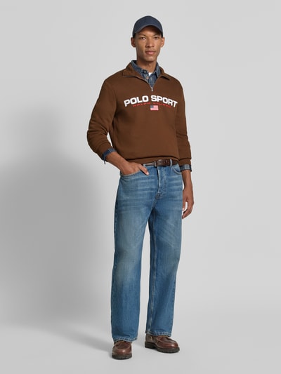 Mannelijk model draagt Relaxed Fit schipperstrui uit katoenmix van Polo Ralph Lauren in bruin, blauwe spijkerbroek, Heren, Ganzkörperansicht von vorne.