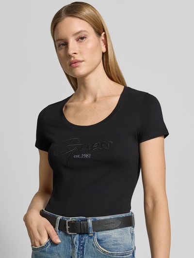 Frauenmodel trägt Damen T-Shirt mit U-Ausschnitt Modell 'SCRIPT' von Guess aus Baumwoll-Elasthan-Mix, körpernaher Schnitt, Label-Stitching, Nahaufnahme Oberkörper.