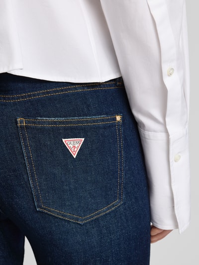 Frauenmodel trägt Flared Jeans mit 5-Pocket-Design von Guess aus Baumwoll-Mix mit Stretch-Anteil, dunkler Jeansstoff, Detailaufnahme Gesäßtasche.