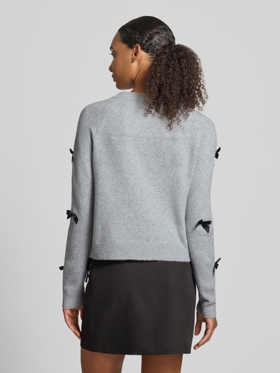 Frauenmodel trägt Regular Fit Pullover mit Raglanärmeln Modell 'NOELLE' von ONLY in Hellgrau mit schwarzen Schleifen, Ganzkörperansicht Rückansicht. Damen Pullover von ONLY