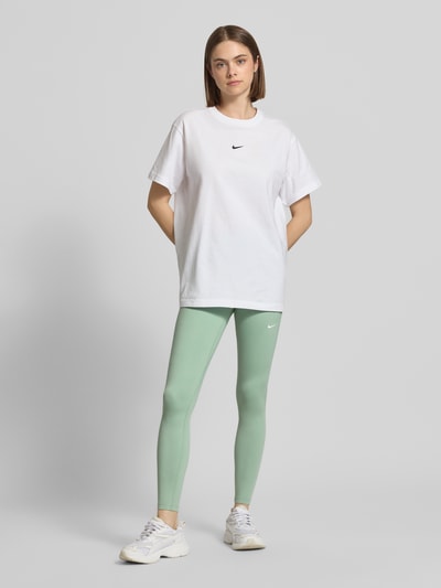 Frauenmodel trägt Leggings mit Logo-Print Modell 'One' von NIKE TRAINING in Mintgrün mit glatter Textur, kombiniert mit weißem Shirt, Ganzkörperansicht von vorne.