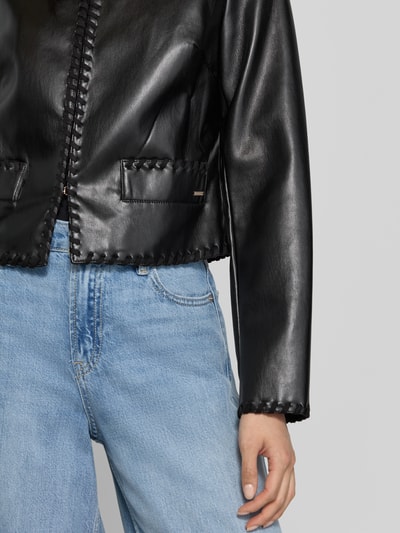 Frauenmodel trägt Jacke in Leder-Optik Modell 'LEONTINE' von GUESS in Schwarz mit Stitchings, kombiniert mit Jeans, Nahaufnahme Oberkörper.