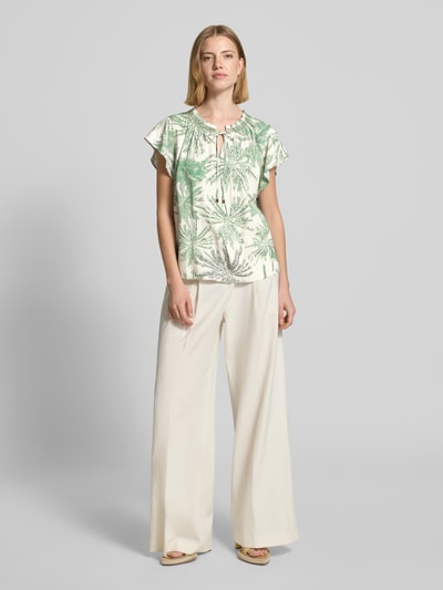 Frauenmodel trägt Loose Fit Bluse aus reiner Viskose von s.Oliver BLACK LABEL mit Optik:Allover-Muster, Passform:Loose-Fit, V-Ausschnitt, Muster:Botanic, Smok-Details, Bindeband, Ärmelform:Kurzarm, Material:reine Viskose, grün-weiß, fließende Textur, Ganzkörperansicht von vorne.