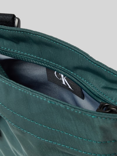 Produktfoto, Crossbody Bag mit Label-Stitching von CK Calvin Klein in Dunkelgrün, Reißverschluss, glatte Textur, Detailaufnahme Hauptfach