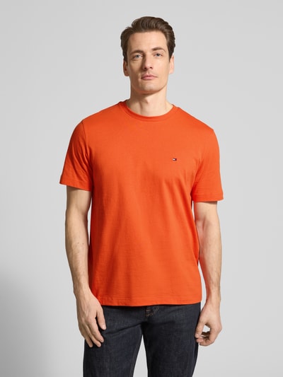 Męski model nosi Regular Fit T-Shirt aus reiner Baumwolle von Tommy Hilfiger, gładki pomarańcz, okrągły dekolt, logo, jersey, Ganzkörperansicht von vorne.