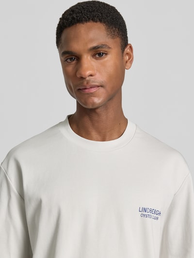 Männermodel trägt Oversized T-Shirt mit Label-Print von Lindbergh in Weiß, Reine Baumwolle, Rundhalsausschnitt, Nahaufnahme Oberkörper.