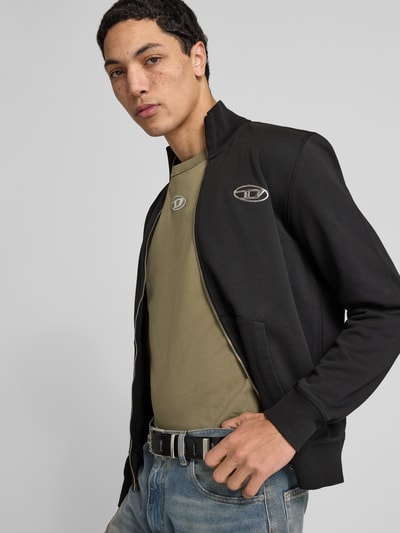 Männermodel trägt schwarze Sweatjacke mit Reißverschluss von Diesel, Reine Baumwolle, Lockerer-Schnitt, Stehkragen, Label-Detail, Nahaufnahme Oberkörper.