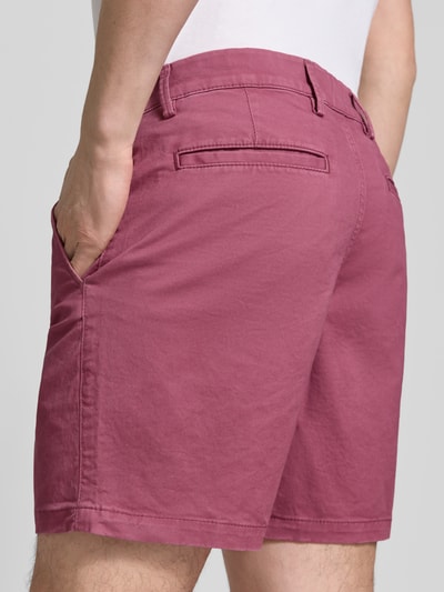 Męski model nosi Shorts mit französischen Eingrifftaschen von GAP, mieszanka bawełny z dodatkiem streczu, krój straight fit, wpuszczane kieszenie, tylne kieszenie, zapięcie na guzik i zamek błyskawiczny, szerokość w rozmiarze 32: 43 cm, długość wewnętrzna nogawki 18 cm, kolor ciemnoróżowy, tekstura gładka, widok z tyłu – ujęcie całej sylwetki.
