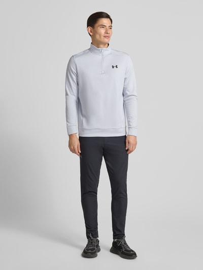 Männermodel trägt Sweatshirt mit Label-Detail von Under Armour in hellem Ton, Stehkragen, Reißverschluss, Lockerer-Schnitt, Ganzkörperansicht von vorne. Rückenlänge bei Größe M: 72 cm, Ärmellänge bei Größe M: 67 cm, gerippte Abschlüsse.