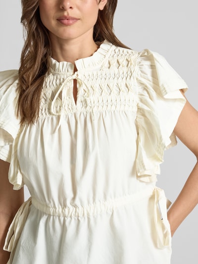 Frauenmodel trägt Bluse mit Serafino-Kragen und Schnürung Modell 'LURA' von YAS, cremefarben, tailliert, Schmetterlingsärmel, Nahaufnahme Oberkörper.