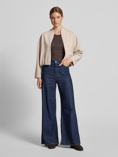 Modelka kobieca nosi Blouson mit Brustleistentasche Modell 'Jamassi' od OPUS, materiał-mix z wiskozą, krój loose fit, beżowe, gładkie, zapięcie na zamek, szwy na ramionach, z kieszenią na piersi, długość tyłu w rozmiarze 36: 53 cm, szerokość ramion w rozmiarze 36: 59 cm, szerokość klatki piersiowej w rozmiarze 36: 62 cm, długość rękawa w rozmiarze 36: 44 cm, widok całej sylwetki z przodu.