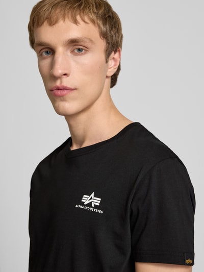 Männermodel trägt T-Shirt mit Logo und Rundhalsausschnitt von Alpha Industries in Schwarz, Reine Baumwolle, Regular-Fit, Nahaufnahme Oberkörper.