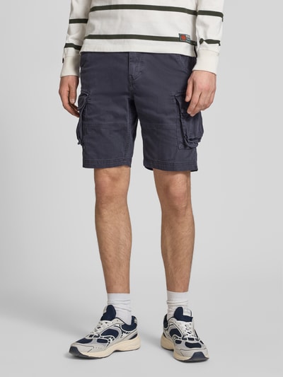 Männermodel trägt Straight Fit Shorts mit Cargo-Taschen Modell 'Core' von Superdry aus Baumwoll-Mix, dunkelblau, Ganzkörperansicht von vorne. Bundweite 42 cm, Innenbeinlänge 23 cm, mit Knopf- und Reißverschluss, Eingriff- und Gesäßtaschen.